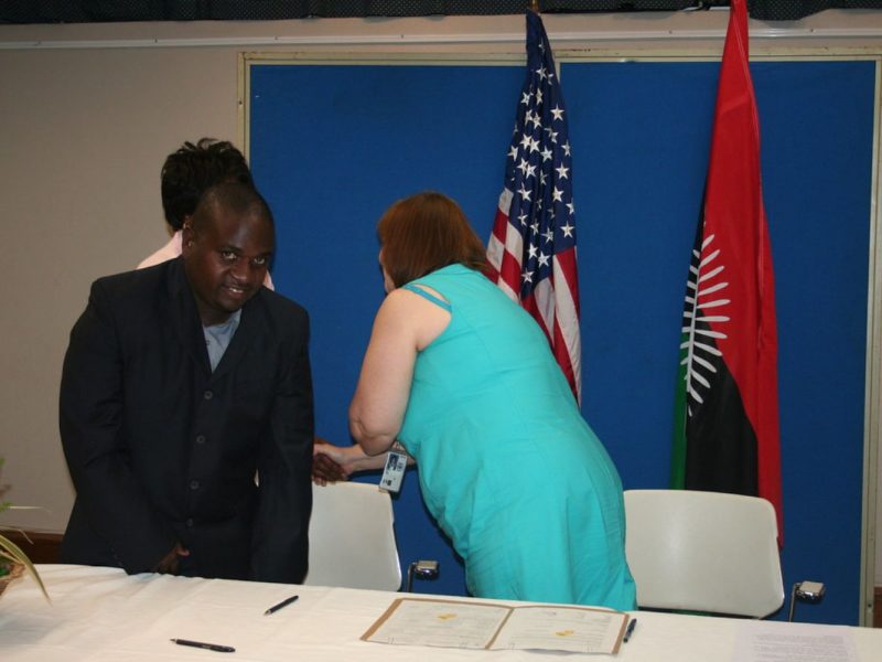 US Chargé d’Affaires Ms Lisa Vickers shakes hands with member of Parliament for the area Ms Jean Sendeza while CRIDOC Director Dr George Mwika Kayange prepares to sign the grant agreement.